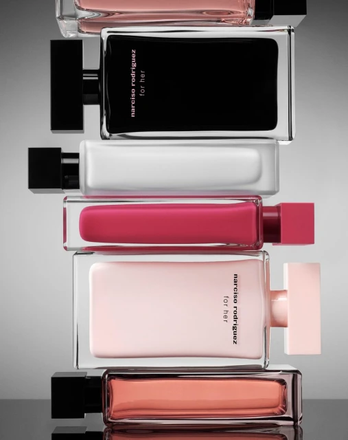 Stacked arrangement of Narciso Rodriguez For Her perfume bottles in various colors including black, white, pink, and peach.