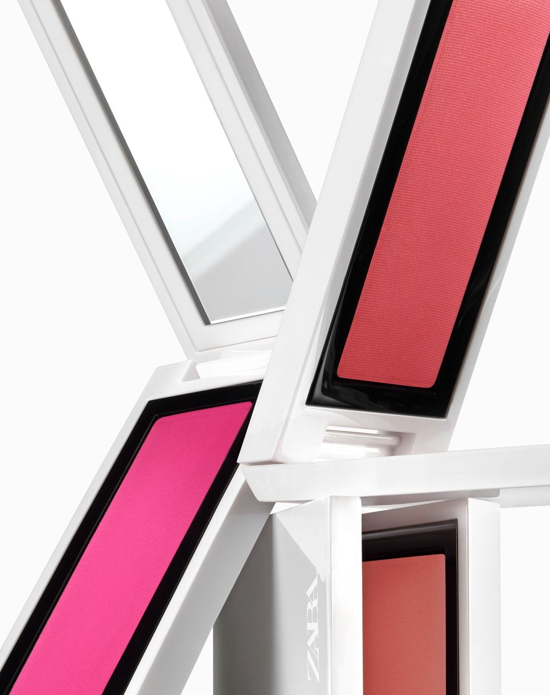 Close-up studio shot of stacked makeup compacts in white cases with pink, coral, and neutral blush shades on a plain background.
