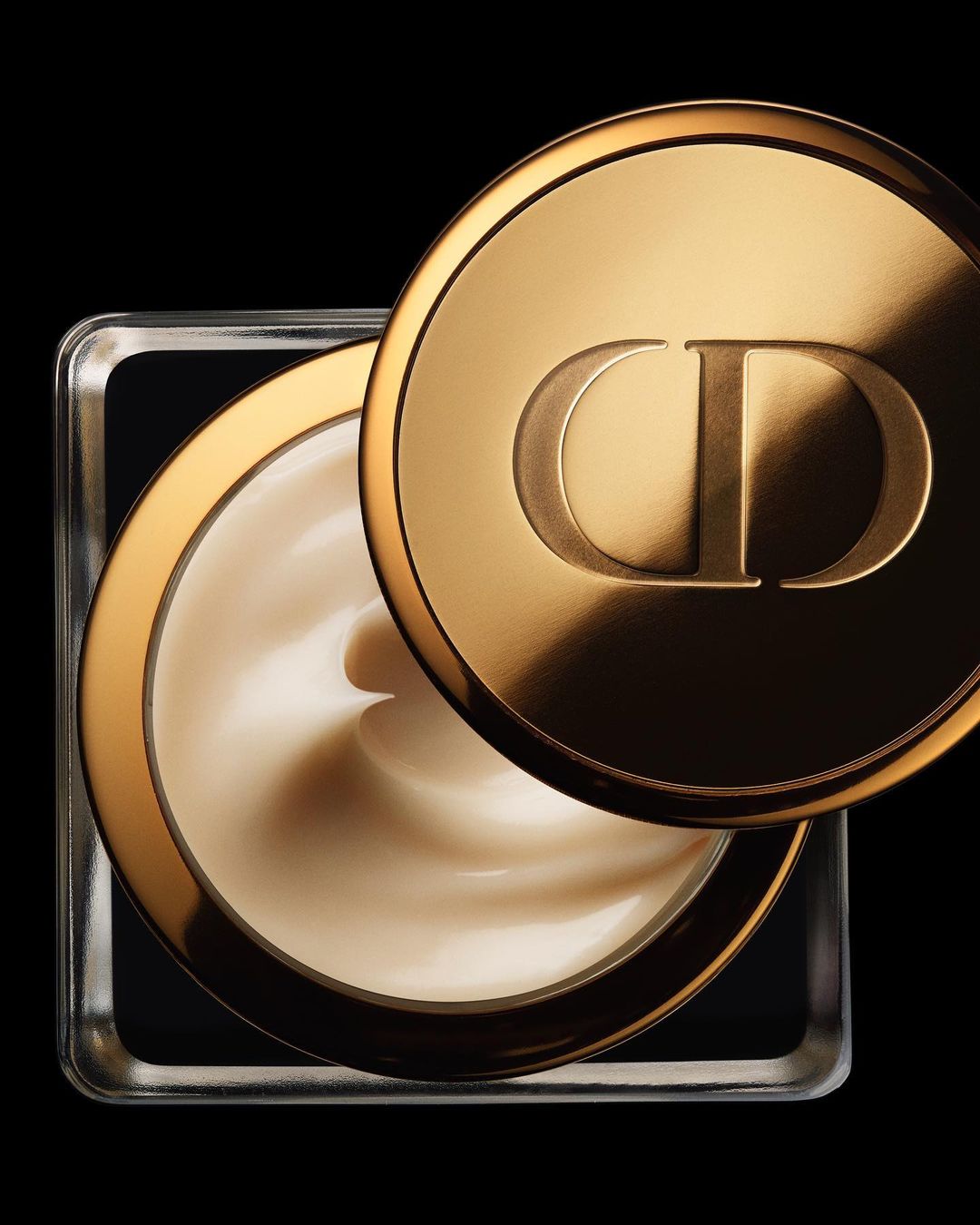 Close-up studio shot of a square glass jar of moisturizing cream with a gold lid bearing the 'CD' logo against a black background.