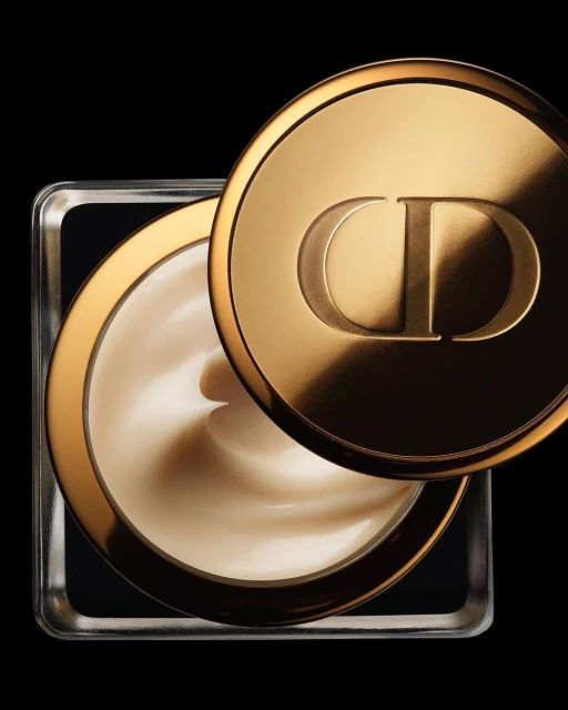 Close-up studio shot of a square glass jar of moisturizing cream with a gold lid bearing the 'CD' logo against a black background.
