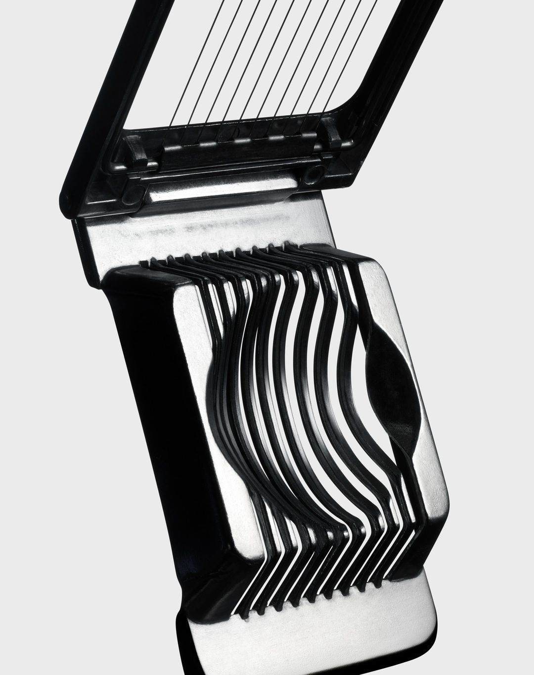 Close-up shot of a black and silver egg slicer, featuring a hinged design with wires for slicing, set against a neutral background.