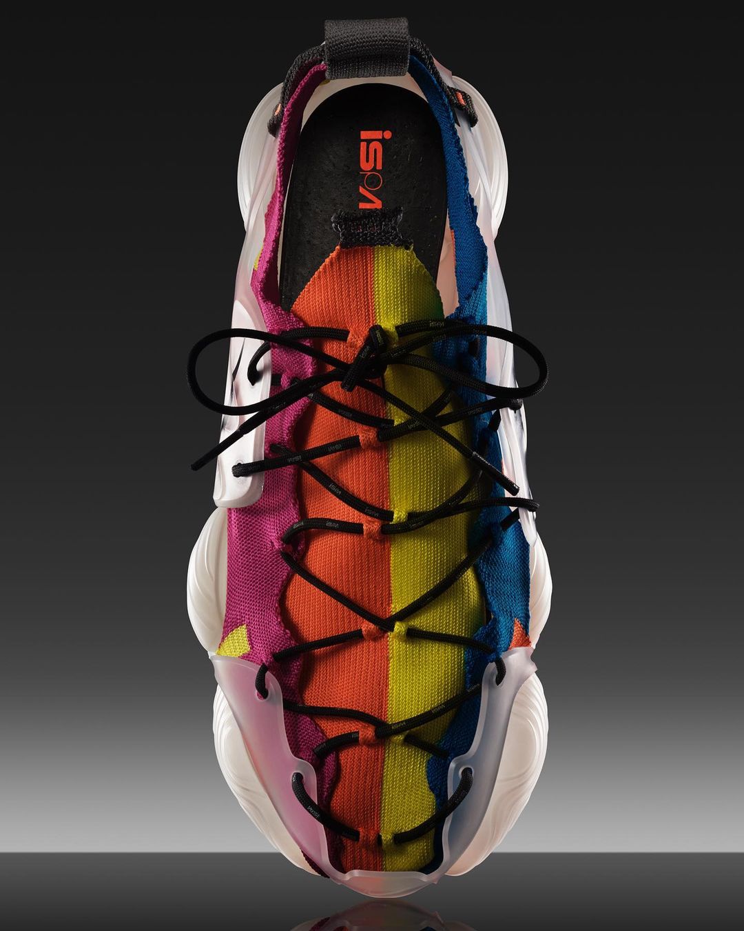 Overhead shot of a modern running shoe with a clear rubber sole and colorful knitted upper with black laces, on a dark gradient background.