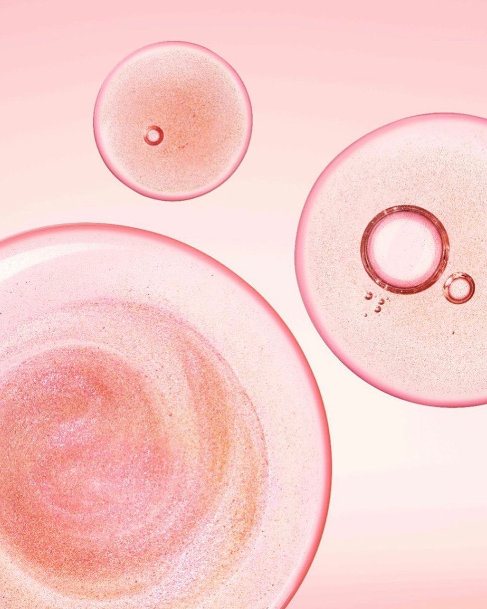 Macro photo of cosmetic serum bubbles floating against a light pink background, showcasing skincare product texture and formulation.