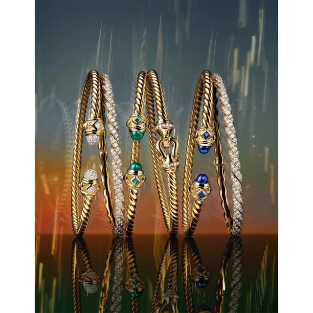Three elegant, gold, twisted bangles with jewel embellishments are displayed against a vibrant, gradient background with reflective surfaces.