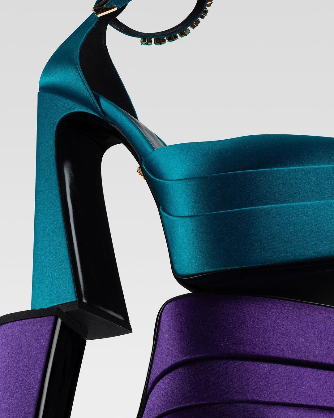 Close-up shot of a platform high heel shoe in teal and purple satin material, featuring a chunky block heel, on a neutral background.