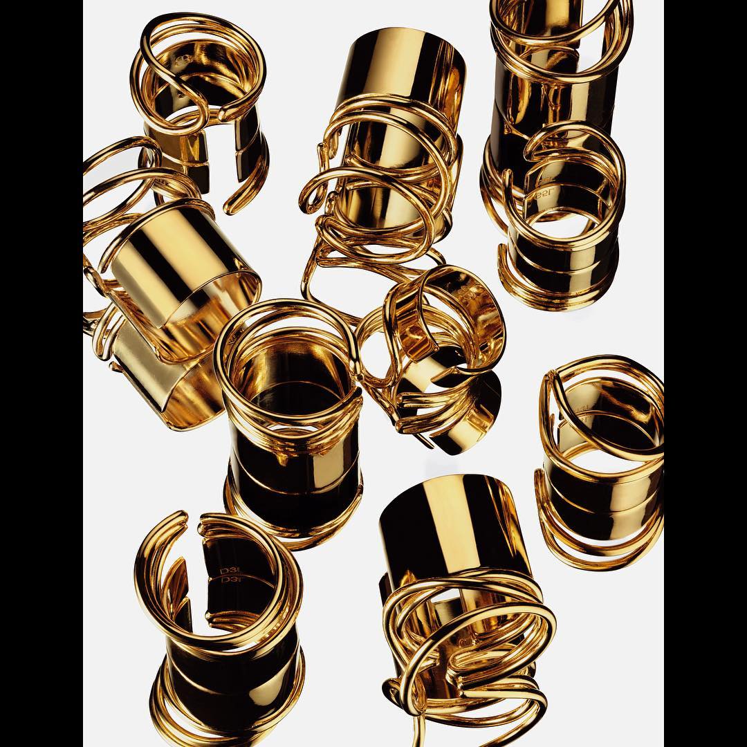 Overhead shot of scattered, shiny, gold-toned metal rings of varying sizes and shapes against a light grey background.