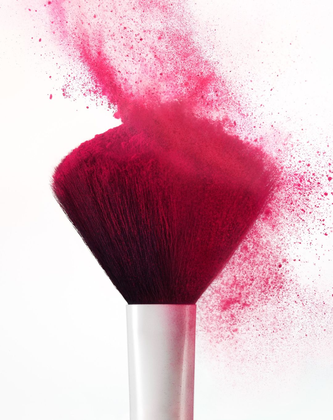 Close-up of a pink makeup brush with powder explosion on a white background, beauty and cosmetics photography.