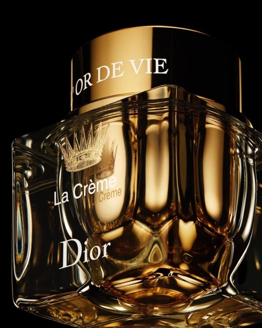 Close-up of a gold and glass Dior La Crème beauty product container with a crown logo on a black background for luxury skincare advertising.