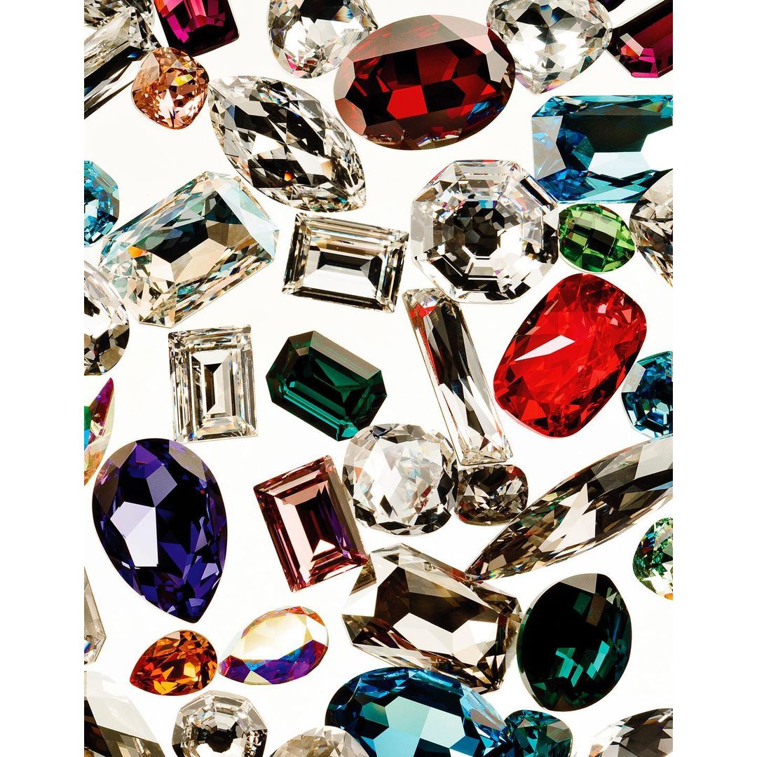 Various shaped gems of different colors against a white background, faceted to catch the light, arranged close together in a random pattern.