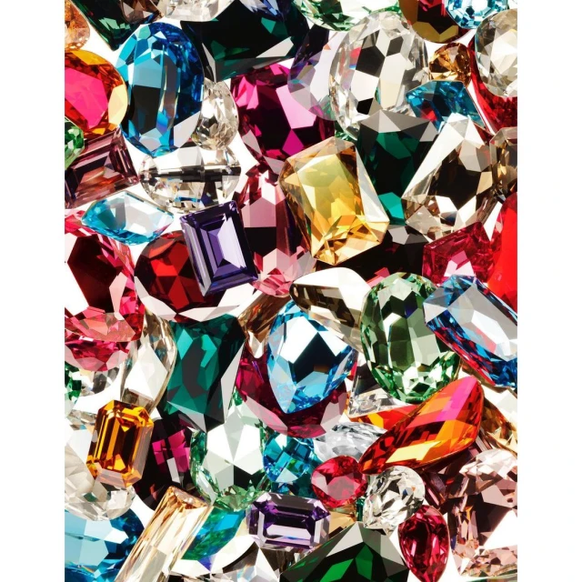 A dazzling array of faceted gemstones in various shapes and colors fills the frame, creating a vibrant and luxurious display of jewelry.