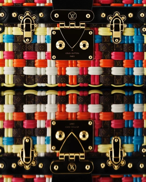 Close-up of a colorful woven Louis Vuitton trunk featuring black leather trim, gold hardware, and vibrant pink, orange, and yellow accents.