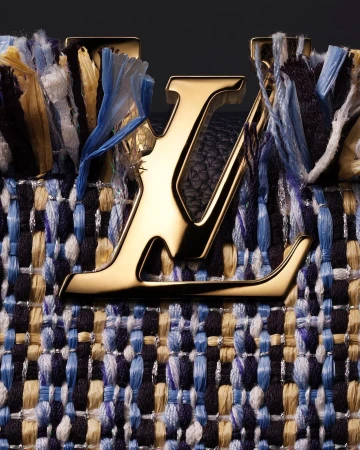 Close-up of a Louis Vuitton handbag featuring a gold logo and a woven tweed design in shades of blue, white, and beige.