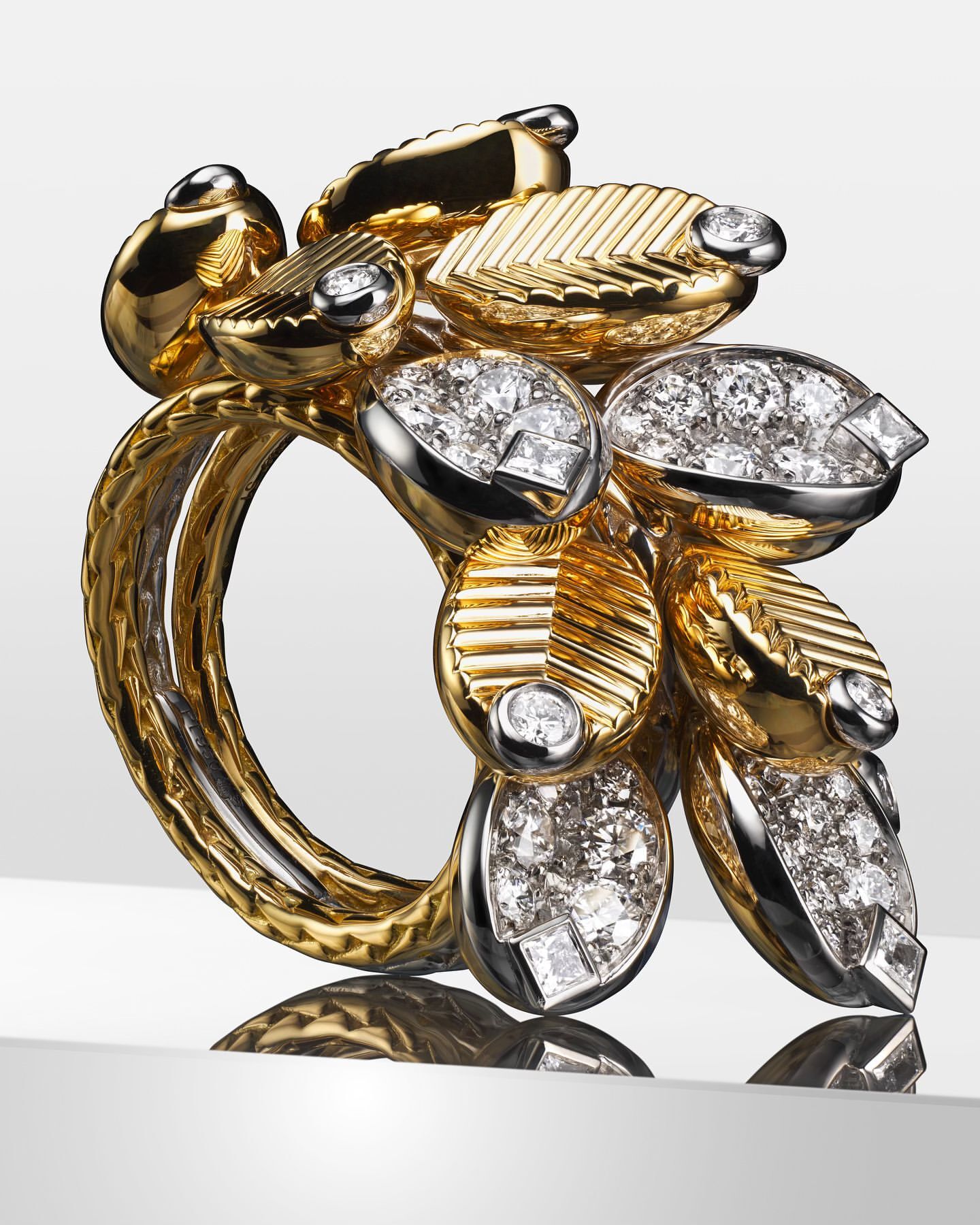 A close-up shot of a gold and silver ring adorned with diamonds, exhibiting a complex design and reflecting on a white surface.