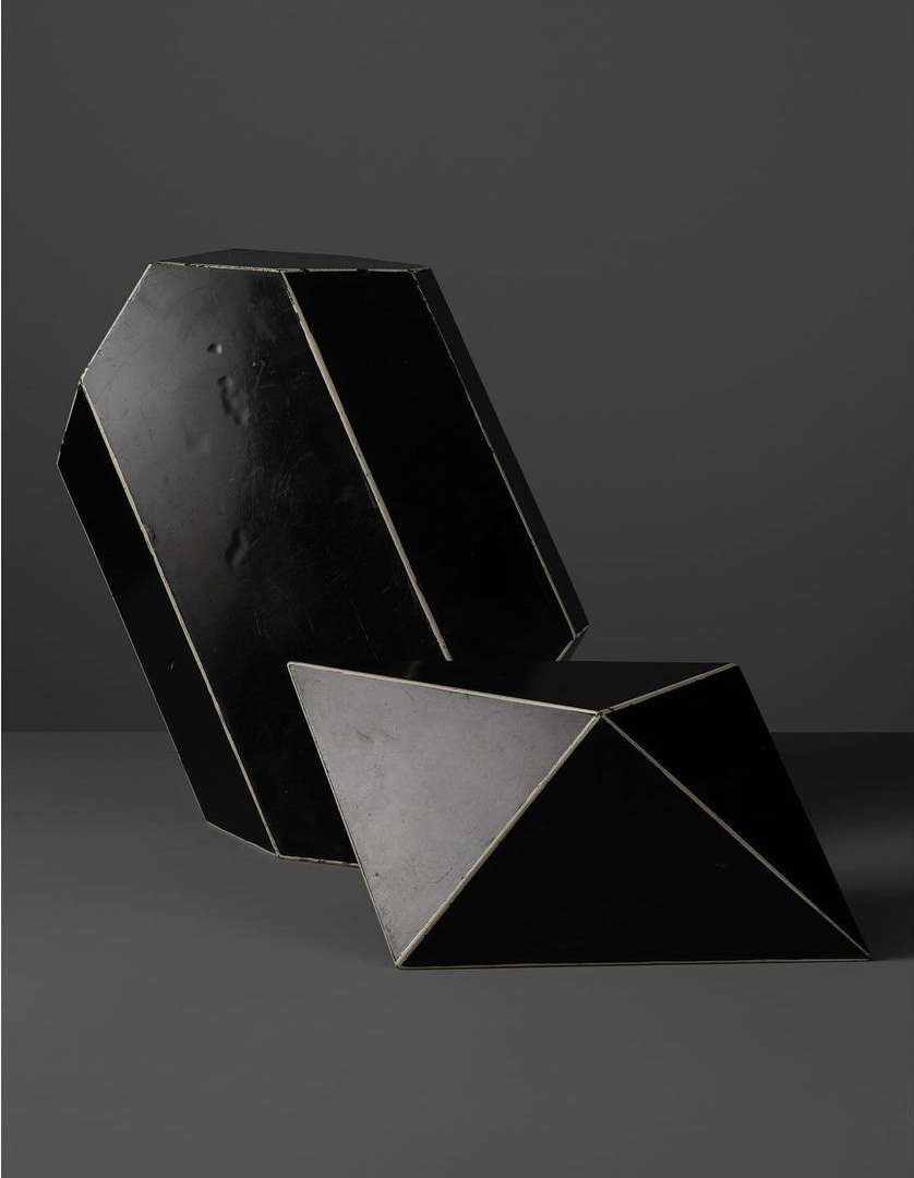 Two geometric black sculptural objects set against a dark grey background in a minimalist still life photograph.
