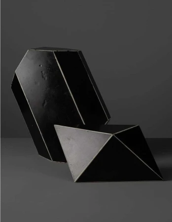 Two geometric black sculptural objects set against a dark grey background in a minimalist still life photograph.