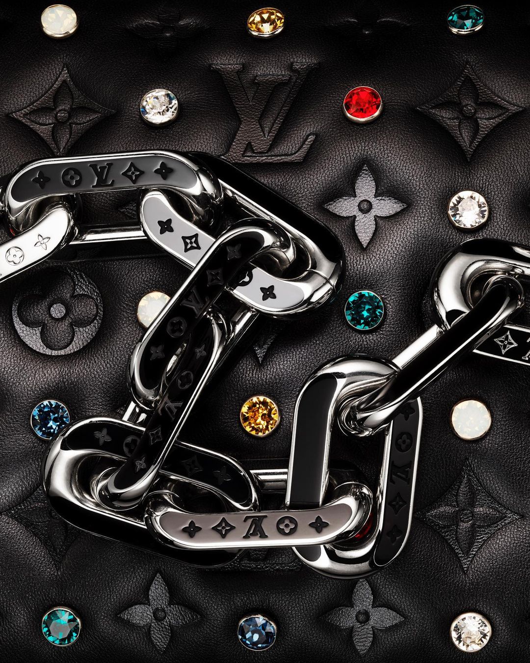 Close-up of a black quilted leather bag featuring a silver chain, colorful jewel embellishments, and a prominent Louis Vuitton logo.
