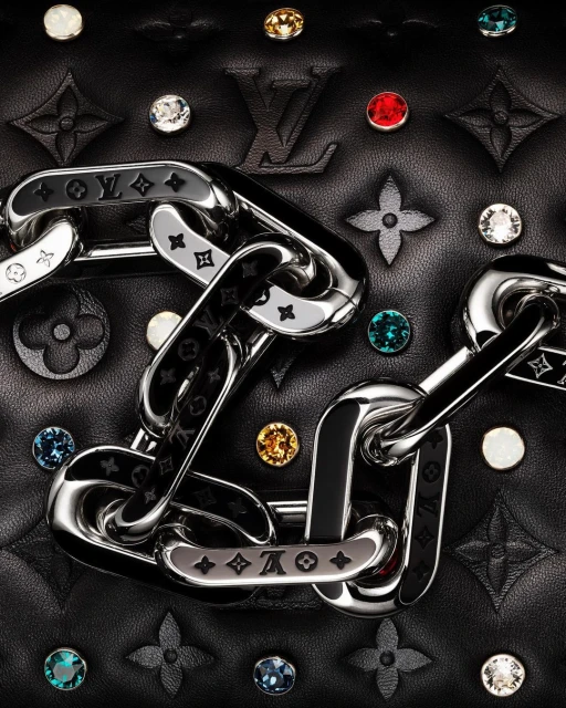 Close-up of a black quilted leather bag featuring a silver chain, colorful jewel embellishments, and a prominent Louis Vuitton logo.