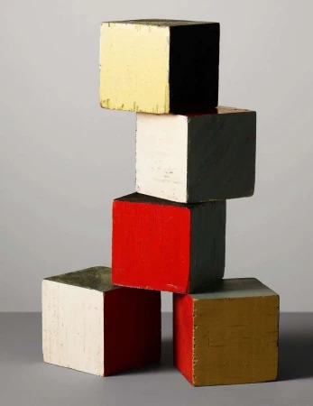 Stack of six colorful wooden blocks, studio shot on a gray background with shadow detail. Yellow, black, white, red, and gold blocks.