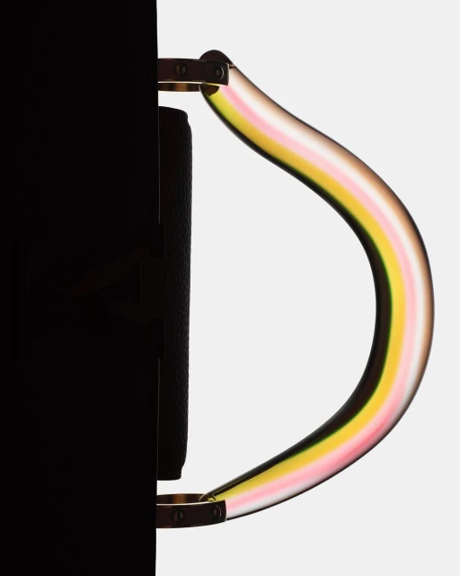 Black handbag with a colorful striped, transparent handle against a light grey backdrop, showing a sleek and modern design.