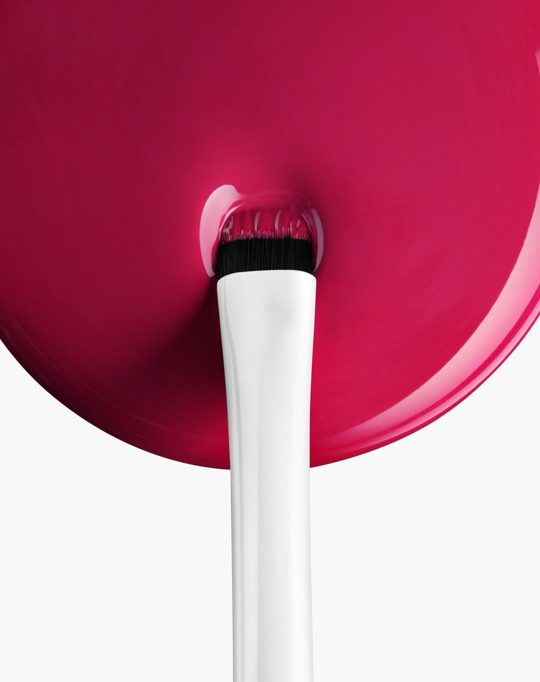 Macro shot of makeup brush applying vibrant pink cosmetic product on a white backdrop, highlighting texture and color.