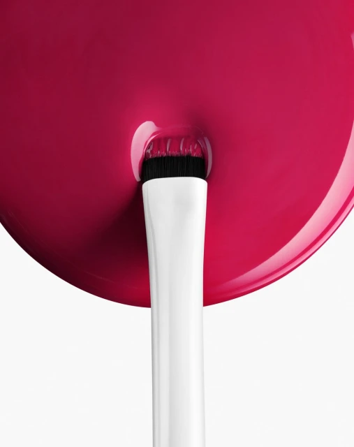 Macro shot of makeup brush applying vibrant pink cosmetic product on a white backdrop, highlighting texture and color.