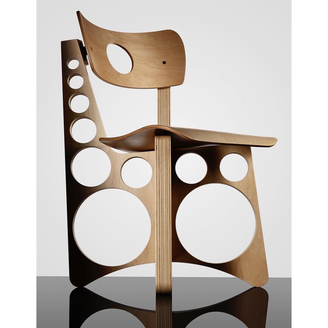 Unique wood chair with circular cutouts is displayed against a white backdrop with a glossy black surface.