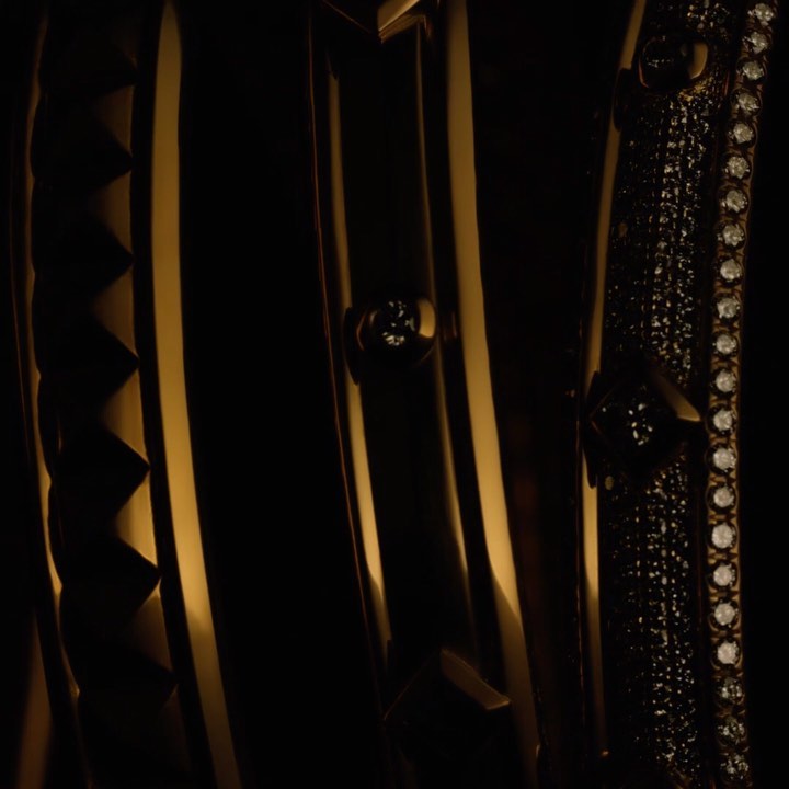 Close-up of golden decorative metalwork featuring geometric patterns, studding, and rows of small jewels against a dark backdrop.