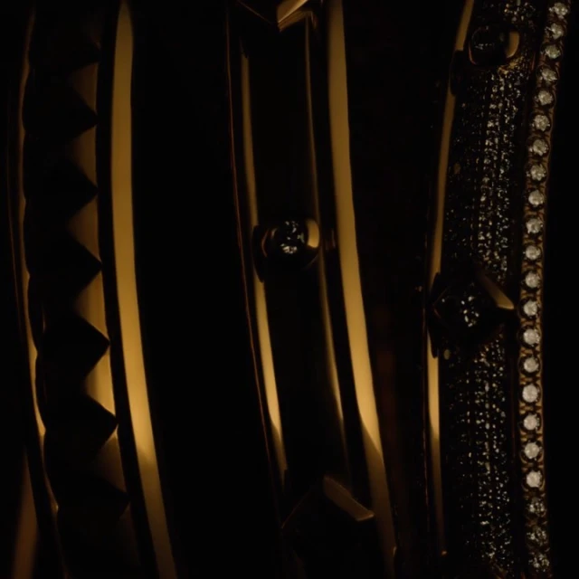 Close-up of golden decorative metalwork featuring geometric patterns, studding, and rows of small jewels against a dark backdrop.