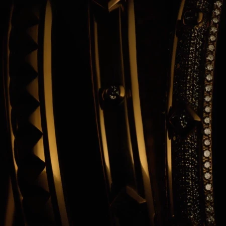 Close-up of golden decorative metalwork featuring geometric patterns, studding, and rows of small jewels against a dark backdrop.