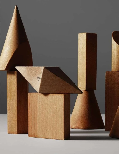 Geometric solids in wood: cones, cubes, pyramids. A collection of vintage wooden 3D geometric shapes on a white surface against a gray backdrop.