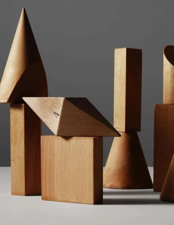 Geometric solids in wood: cones, cubes, pyramids. A collection of vintage wooden 3D geometric shapes on a white surface against a gray backdrop.