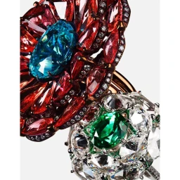 Close-up product photography of two ornate gemstone rings featuring red, blue, green, and clear diamonds on a white background.