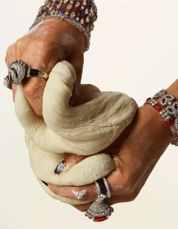 Close-up of hands covered in flour kneading bread dough while wearing heavy diamond and gemstone jewelry shot by Robin Broadbent.