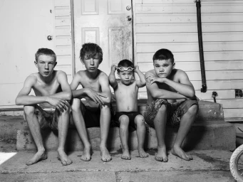 Black and white portrait of four shirtless boys sitting on outdoor steps in Amsterdam by photographer Robin De Puy.