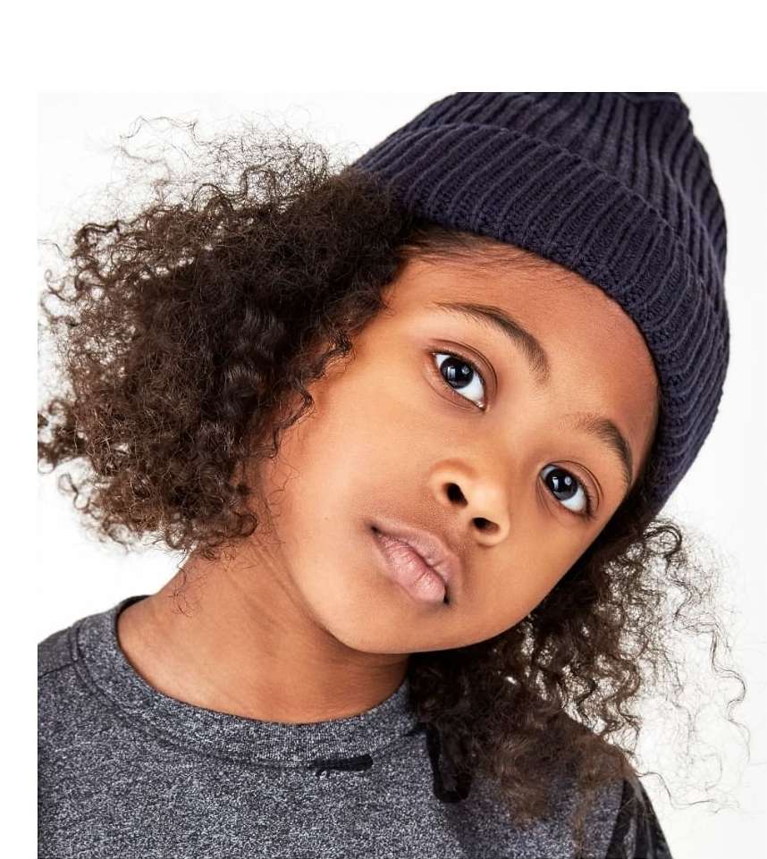 Portrait of a child wearing a dark beanie and grey t-shirt against a plain white studio background.
