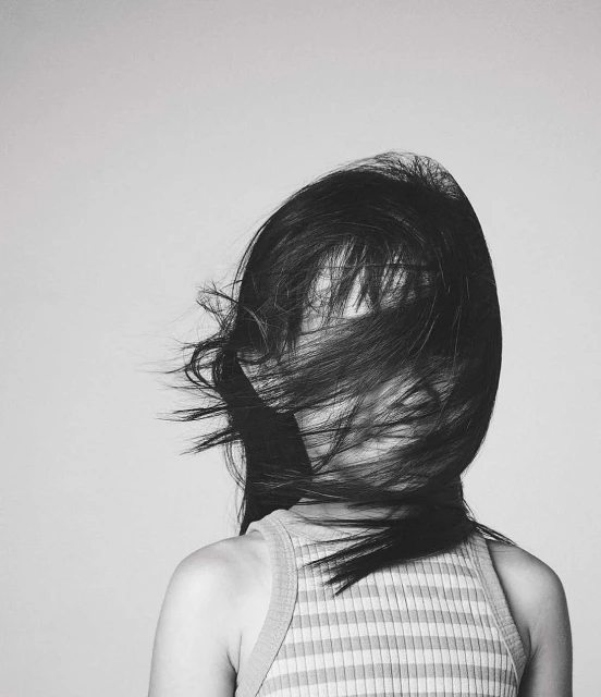 Monochromatic portrait of a woman with long hair partially obscuring her face, wearing a striped top against a light grey backdrop.