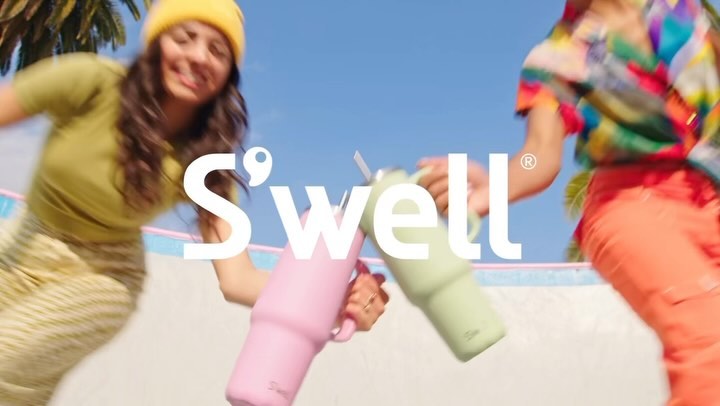 Two people cheers with S'well water bottles on a sunny day. Palm tree in background. S'well logo superimposed on the foreground.