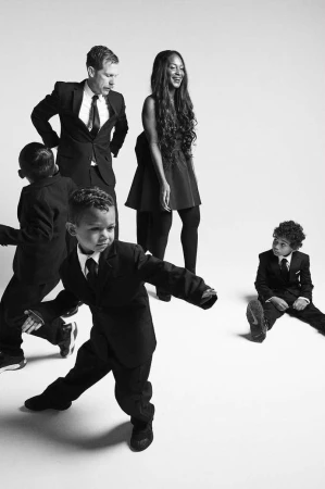 Group of adults and children in formal black suits against a white studio background captured in a dynamic portrait by Robyn Breen Shinn.