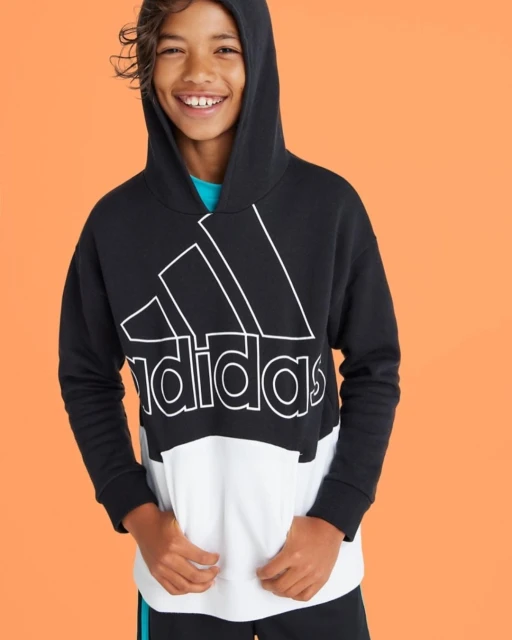 Smiling child wearing an Adidas black-and-white hoodie, captured in a studio shot against an orange background. Youthful fashion.