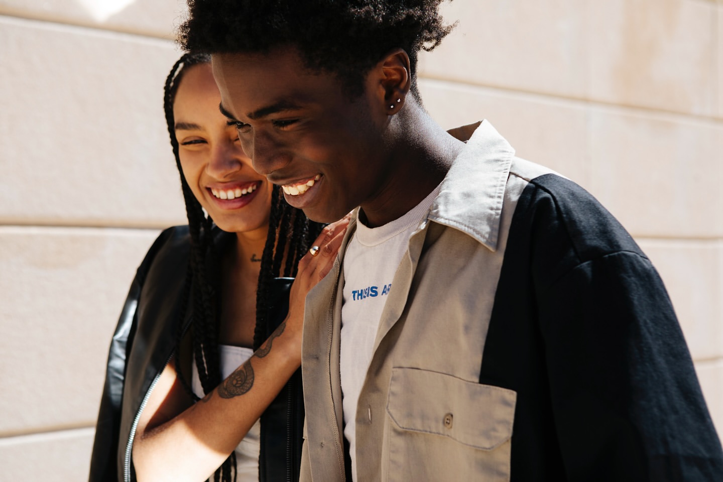 A smiling Black man and woman pose together outdoors, the man in a two-tone tan and black shirt, the woman in a black jacket.