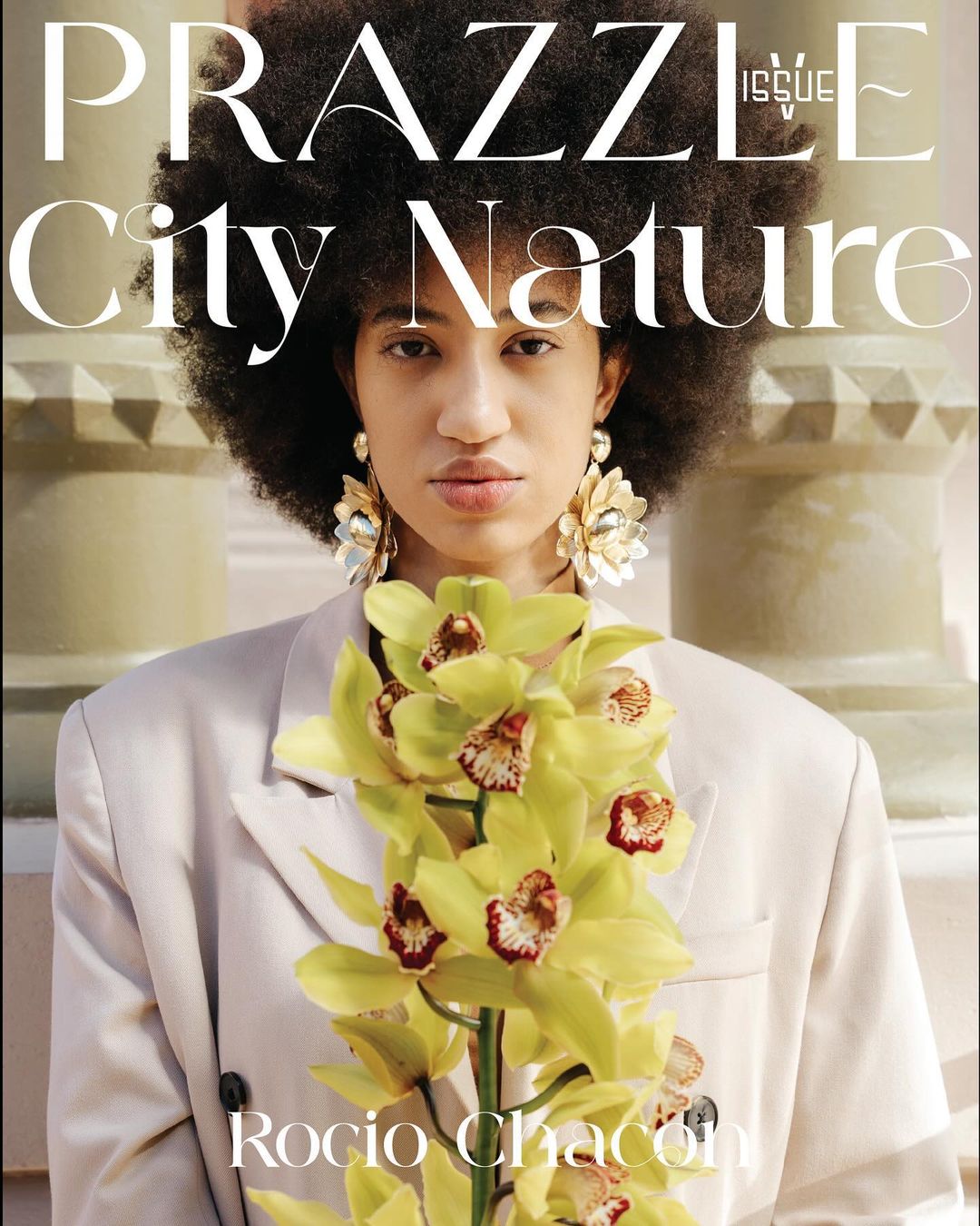 Magazine cover featuring an adult woman with afro, wearing a blazer and flower earrings. She is holding orchids in front of pillars.
