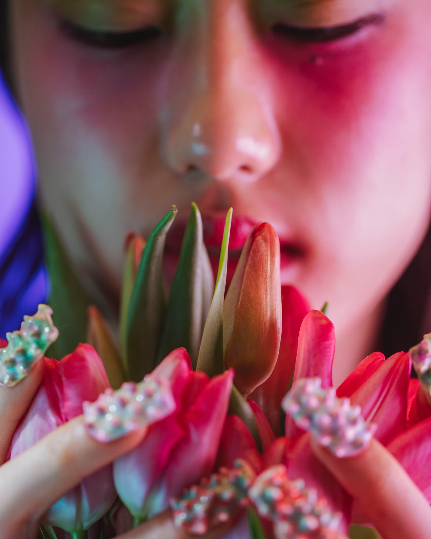 Close-up of a person holding vibrant pink and red tulips, face partially obscured by flowers, artistic lighting, embellished fingernails.