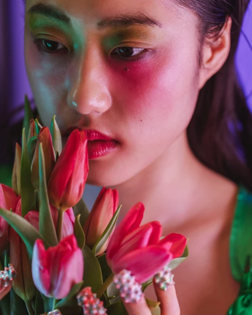 Close-up of Asian woman with striking makeup holding tulips, creating a vibrant and intimate fashion beauty portrait.