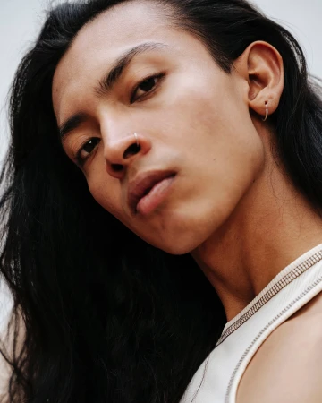 Close-up portrait of a young man with long dark hair wearing a white top and a nose ring by Rocio Chacon