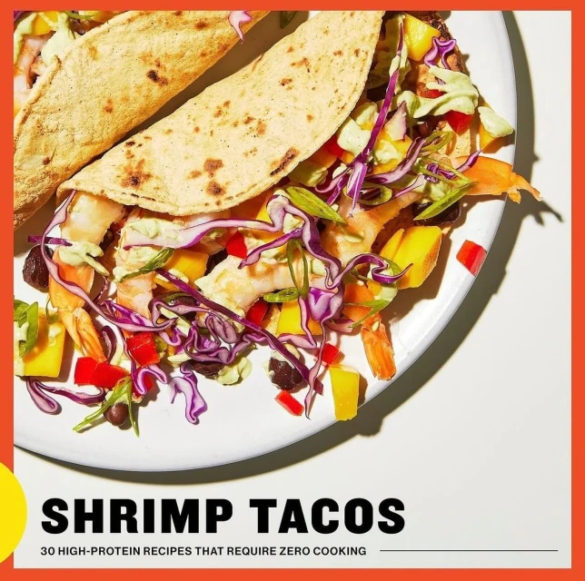 Overhead shot of two shrimp tacos with mango, cabbage, and purple cabbage on a white plate with an orange and yellow border.