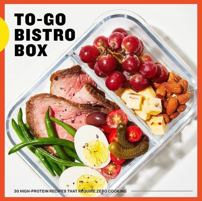 High-protein bistro box: sliced steak, green beans, boiled eggs, grapes, cheese cubes, pickles, cherry tomatoes and almonds in a clear container.