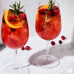 Two wine glasses filled with red cocktail garnished with orange slices, cranberries, and rosemary sprigs.