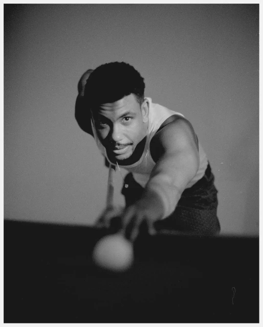 Monochrome portrait of a man with a ball, aiming at a billiards table in a photography studio setting with soft, even lighting.