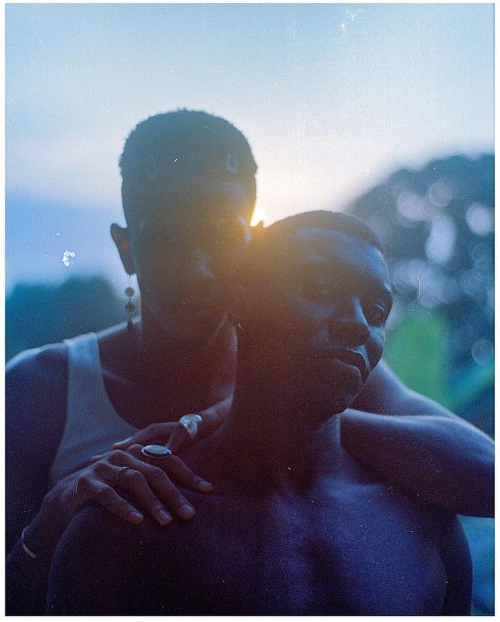 Outdoor portrait of a Black couple at dusk, embracing against a blurred background of trees and a sunset sky.