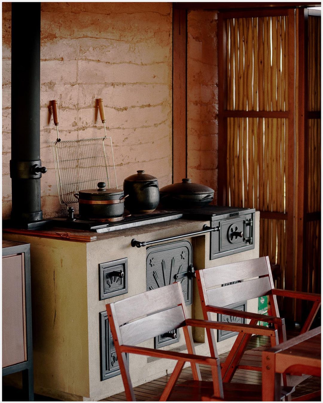 Indoor kitchen featuring a wood-burning stove with pots, accompanied by two wooden chairs and a textured wall in a warm, inviting ambiance.